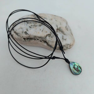 May include: A black cord necklace with a teardrop-shaped abalone shell pendant. The shell has iridescent green, blue, and gold colors.