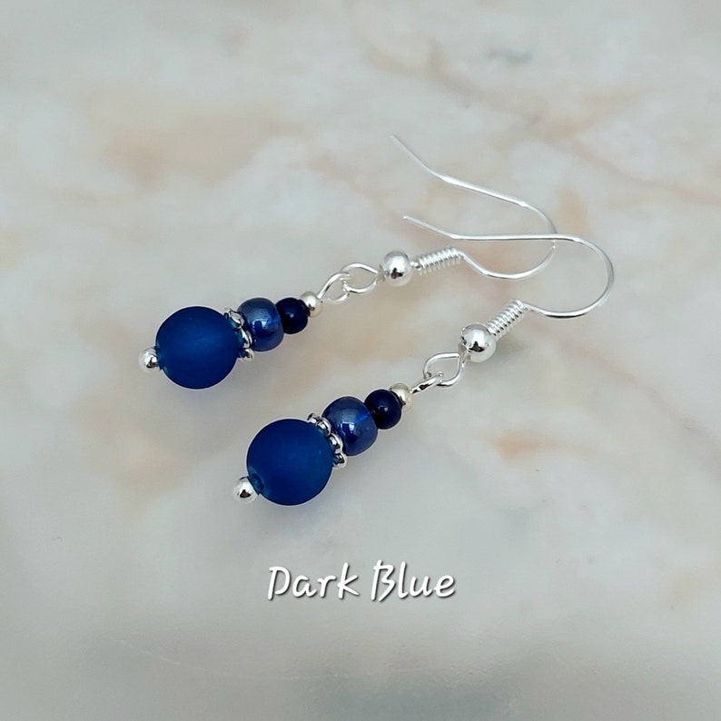 May include: A pair of silver dangle earrings with dark blue glass beads. The earrings have a simple design and are perfect for everyday wear.