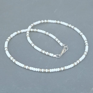Peut inclure: Un collier de perles blanches avec un fermoir argent&eacute;. Le collier est compos&eacute; de petites perles rondes et mesure environ 45 cm de long.