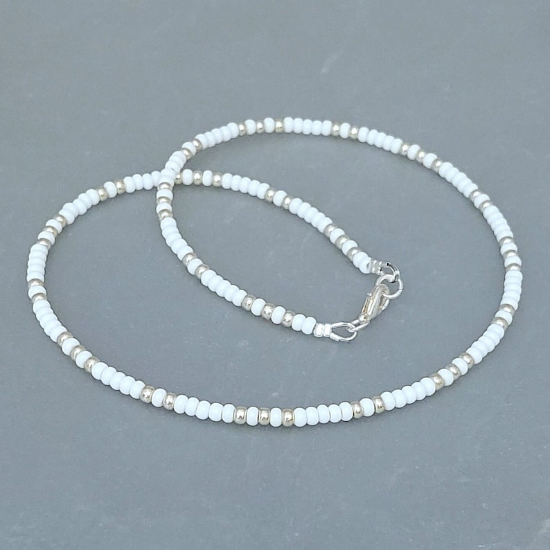 Peut inclure: Un collier de perles blanches avec un fermoir argent&eacute;. Le collier est compos&eacute; de petites perles rondes et mesure environ 45 cm de long.