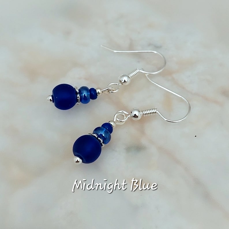 May include: A pair of silver dangle earrings with a midnight blue glass bead and smaller blue beads. The earrings are labelled "Midnight Blue".