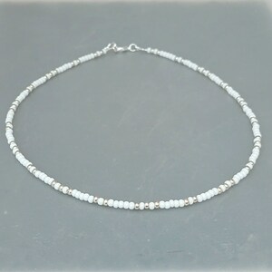 Peut inclure: Un collier d&eacute;licat en perles blanches avec un fermoir argent&eacute;. Le collier est compos&eacute; de petites perles rondes et est parfait pour &ecirc;tre superpos&eacute;.