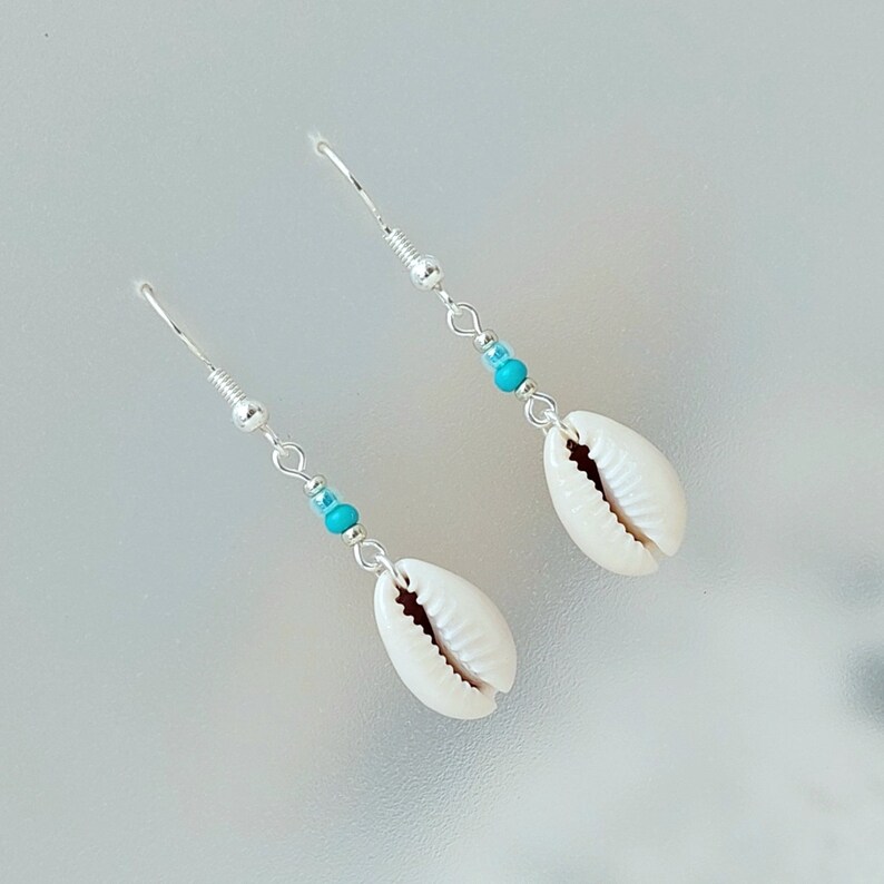 May include: A pair of silver earrings with turquoise beads and white shell charms.