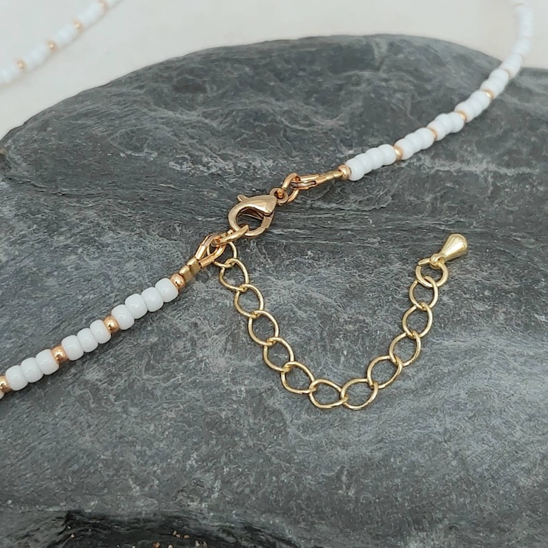 Peut inclure: Un collier de perles blanches avec un fermoir et une cha&icirc;ne d'extension dor&eacute;s.
