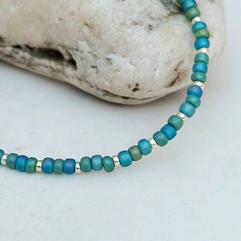 May include: A delicate bracelet made with small, iridescent blue and green beads interspersed with silver beads.