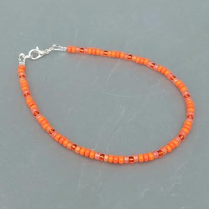 May include: A delicate orange and peach beaded bracelet with a silver clasp.