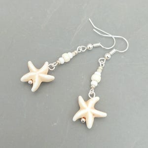 May include: A pair of silver earrings with white beads and a starfish charm. The starfish are a light beige colour.