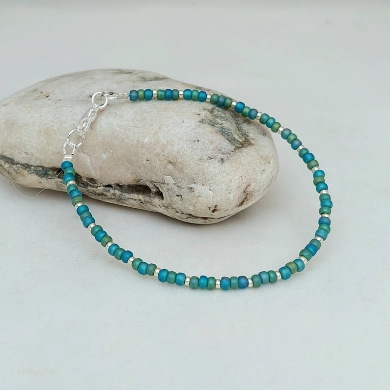 May include: A delicate bracelet made with tiny teal and silver beads. The bracelet is strung on a silver chain with a lobster clasp.