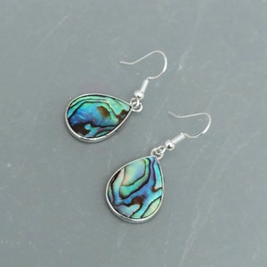 May include: A pair of teardrop earrings featuring iridescent abalone shells set in silver-coloured metal. The abalone shells display a mix of blue, green, and brown hues. The earrings have a simple hook design.