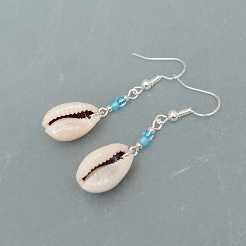 May include: A pair of silver earrings with a white cowrie shell and blue beads hanging from each earring.