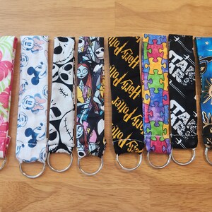 May include: A set of ten colorful keychains with various designs, including a floral pattern, Mickey Mouse, Jack Skellington, Harry Potter, a puzzle, Star Wars, and a sun and moon design. Each keychain has a silver metal ring.
