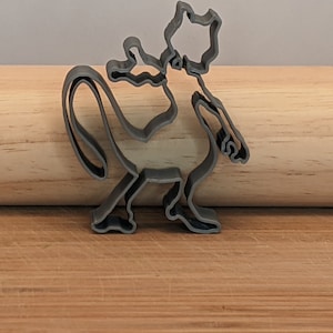 May include: A gray metal cookie cutter shaped like a cartoon cat with a long tail.