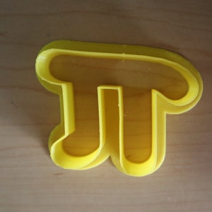 May include: A yellow plastic cookie cutter shaped like the mathematical symbol pi.