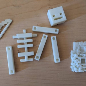 Puede incluir: Un conjunto de bloques de construcci&oacute;n de pl&aacute;stico blanco, que incluye un bloque cuadrado con una cara, un bloque curvo, un bloque con un patr&oacute;n de cuadr&iacute;cula y un bloque con una textura rugosa.