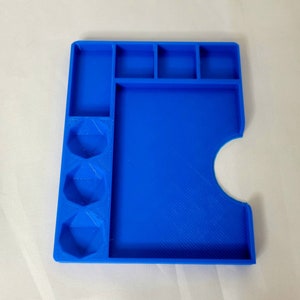 May include: A blue plastic tray with compartments for dice and a larger area for rolling. The tray has a cutout for a card or game piece.