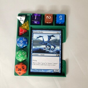 May include: A green plastic dice tray with compartments for different sized dice. The tray has a card slot for a Magic: The Gathering card, which is showing the card "Azure Drake". The card text reads "Flying. Move so than "saorum" or "pirate," "drake" is the word a sailor least wants to hear."