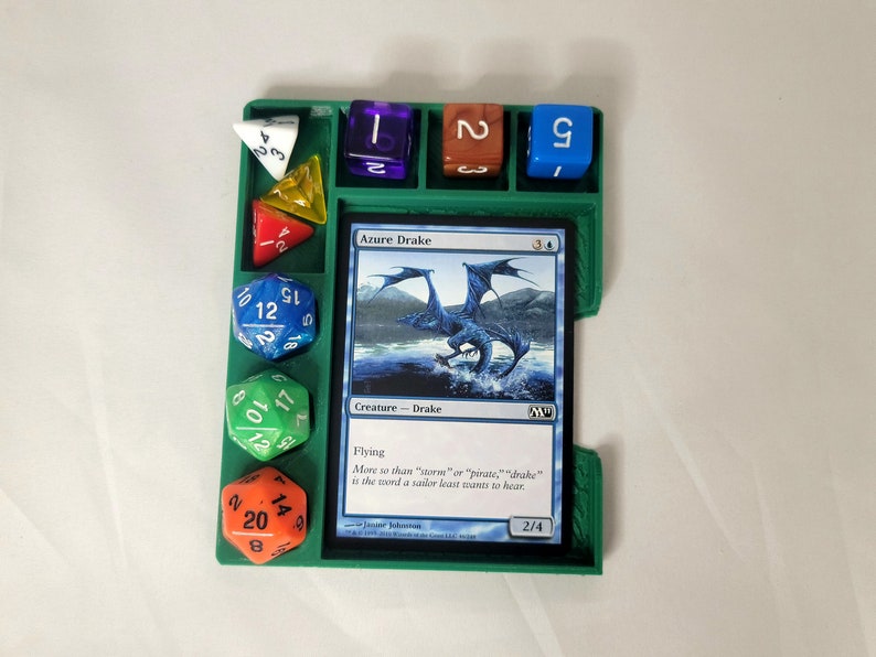 May include: A green plastic dice tray with compartments for different sized dice. The tray has a card slot for a Magic: The Gathering card, which is showing the card "Azure Drake". The card text reads "Flying. Move so than "saorum" or "pirate," "drake" is the word a sailor least wants to hear."