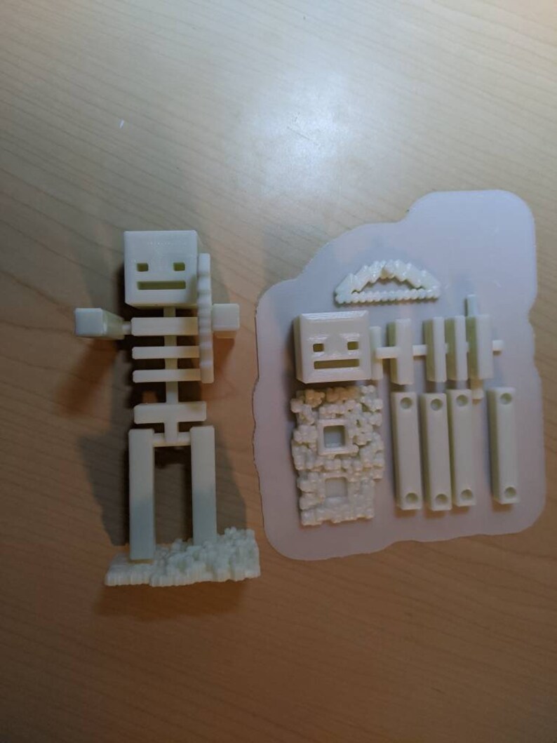 Puede incluir: Un modelo de esqueleto de pl&aacute;stico blanco impreso en 3D con una espada. El modelo est&aacute; ensamblado y listo para jugar. El modelo est&aacute; sobre una superficie de madera.
