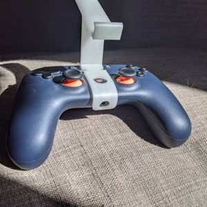 May include: A dark blue video game controller with two orange buttons and a white stand.