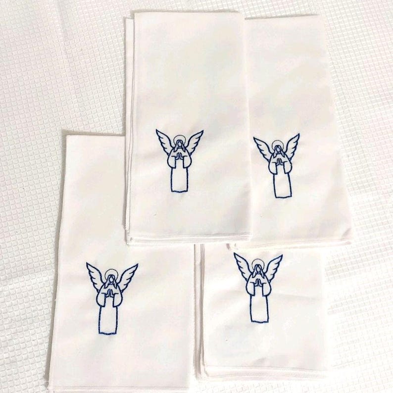 Może przedstawiać: Pięć białych ręcznik&oacute;w z niebieskim haftowanym wzorem anioła. Ręczniki są złożone i ułożone na białej, teksturowanej powierzchni. Anioł ma rozłożone skrzydła i złożone dłonie.