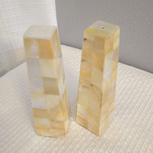 Puede incluir: Un juego de dos saleros y pimenteros hechos de azulejos de nácar iridiscente. Los saleros son rectangulares y tienen un color amarillo claro y blanco.
