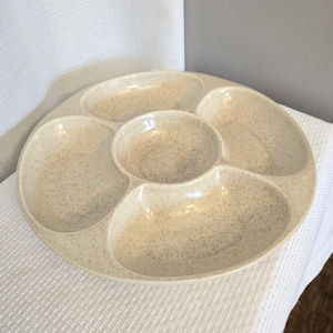 Könnte beinhalten: Eine beige Keramik-Servierplatte mit fünf separaten Fächern. Die Platte hat ein gesprenkeltes Muster.