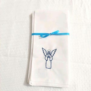 Może przedstawiać: Stos białych chusteczek związanych jasnoniebieską wstążką. Każda chusteczka ma niebieski haft z aniołem. Anioł ma złożone dłonie i skrzydła. Tło to biała, teksturowana powierzchnia.