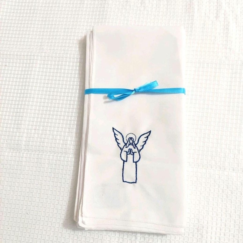 Może przedstawiać: Stos białych chusteczek związanych jasnoniebieską wstążką. Każda chusteczka ma niebieski haft z aniołem. Anioł ma złożone dłonie i skrzydła. Tło to biała, teksturowana powierzchnia.