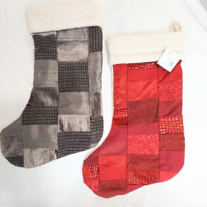 May include: Two Christmas stockings with patchwork designs. One is gray with various textures, and the other is red with different patterns. Both have white, fluffy cuffs.