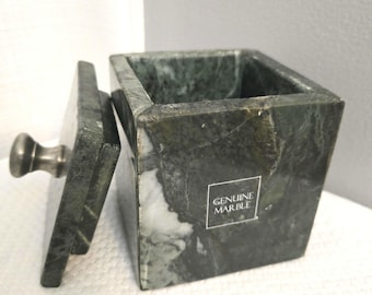 May include: A square, green marble box with a lid and a silver knob. The lid is slightly ajar, revealing the interior. The box has a "GENUINE MARBLE" sticker on the side. The marble has a natural, veined pattern.