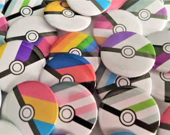 May include: A collection of colorful round buttons with a white background and a black and white design of a Pokeball. The buttons feature various pride flags, including the rainbow, transgender, bisexual, and pansexual flags.