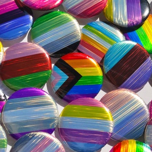 Op de afbeelding: Een verzameling kleurrijke, iriserende pinnen met verschillende pride-vlaggen, waaronder de transgender-, bi- en panseksuele vlag.