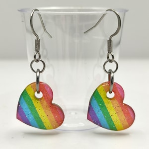 Op de afbeelding: Regenboogvormige hartvormige oorbellen met glitteraccenten. De oorbellen zijn gemaakt van metaal en hebben een zilveren afwerking.