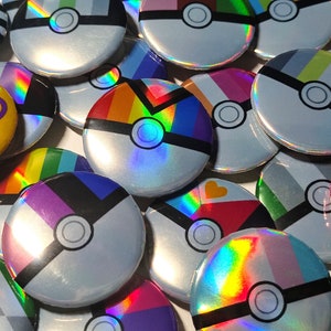 Peut inclure: Une collection de boutons ronds, irisés et colorés avec une variété de motifs, dont un arc-en-ciel, une Poké Ball et un drapeau arc-en-ciel. Les boutons mesurent environ 5 cm de diamètre.