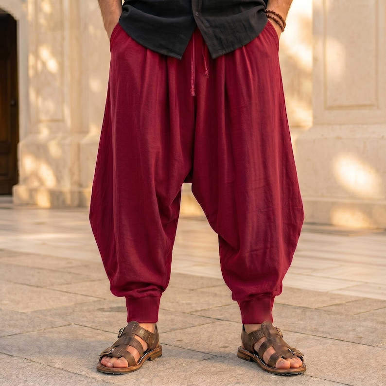 K&ouml;nnte beinhalten: Dunkelrote Pluderhose mit lockerer, volumin&ouml;ser Passform, geraffter Taille und eng zulaufenden Beinabschl&uuml;ssen mit B&uuml;ndchen. Die Hose wird mit einem schwarzen Hemd und braunen Ledersandalen kombiniert und zeigt eine entspannte Silhouette.