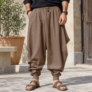 Peut inclure: Pantalon marron ample avec une coupe à entrejambe bas, une taille élastique avec cordon de serrage et des chevilles resserrées. Ce pantalon possède des poches latérales et est fabriqué dans un tissu uni à la finition mate.