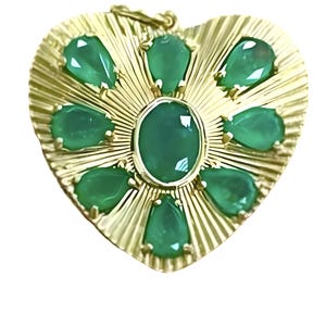 May include: A gold-colored heart-shaped pendant with a sunburst design. The pendant is adorned with a central oval green gemstone, surrounded by eight teardrop-shaped green gemstones. The pendant has a loop at the top for a chain.