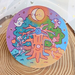 Op de afbeelding: Een ronde sticker met een grillige illustratie. Een lachende boom staat centraal, met een regenboog en een spiraalvormig ontwerp. Een skelet, een geest en een fee zijn ook afgebeeld. De achtergrond bevat een lachende zon en maan.
