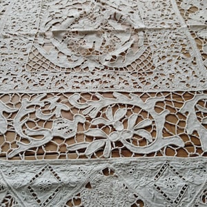 May include: A white lace tablecloth featuring intricate floral patterns and a delicate, openwork design. The tablecloth is crafted from fine, white thread and has a vintage, antique appearance.