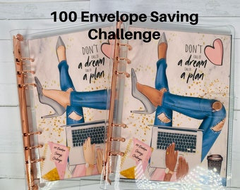May include: A clear plastic binder with a gold metal ring mechanism. The binder has two pages with a colourful illustration of a woman sitting on a laptop with the text "Don't call it a dream, call it a plan". The pages also have the text "100 Envelope Saving Challenge".