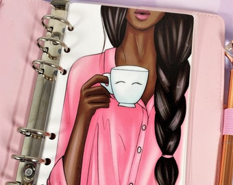 May include: A pink button-down shirt with a white cup featuring a smiley face. The person in the image has long dark brown hair styled in a braid.