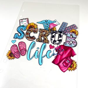 May include: A clear planner insert with the words "SCRUB LIFE" in colorful, patterned letters. The design includes medical symbols, pink clogs, a red scrub top, and sunflowers. The insert has three holes for binding.