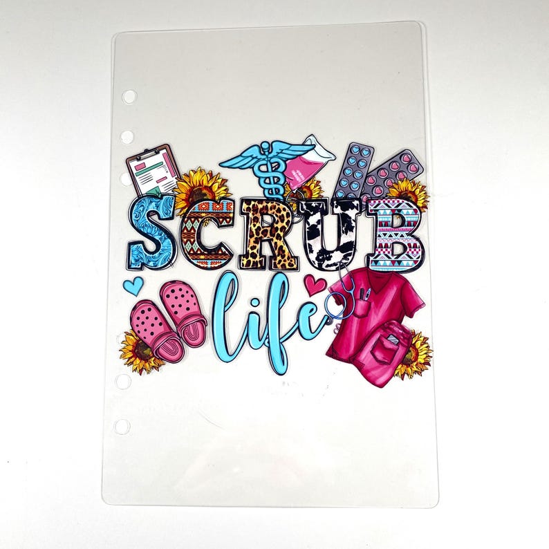 May include: Clear planner insert with the words "SCRUB LIFE" in colorful letters. The design includes medical symbols, sunflowers, pink clogs, a pink scrub top, and pills.