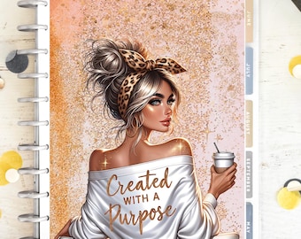 Puede incluir: Un planificador con una ilustración de una mujer rubia de ojos azules, que lleva una camiseta blanca con los hombros descubiertos con el texto "Created with a Purpose". Sostiene una taza de café. El fondo es rosa y dorado.