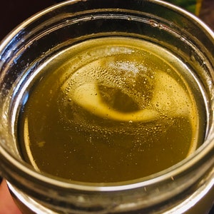 May include: A glass jar filled with a light green liquid. The liquid has a cloudy appearance with small bubbles throughout.