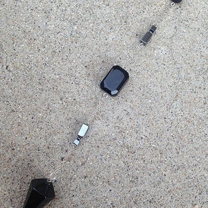 Peut inclure: Un pendule en cristal noir avec une chaîne argentée et des perles noires. Le pendule est en forme de pointe et a une perle de cristal rectangulaire.