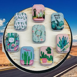 May include: Eight small, rectangular metal tins with different cactus-themed designs. The tins have white lids and are decorated with various colors, including pink, green, blue, and yellow. The designs include cacti, flowers, and text such as "Furry Cactus", "Wander Lust", and "Don't Touch Me".