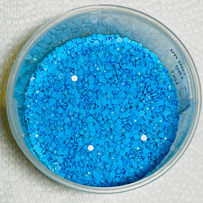 May include: A clear plastic bowl filled with a large quantity of small, light blue, round, flat, iridescent rhinestones.