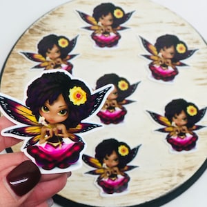 Peut inclure: Un ensemble de huit autocollants de fées colorés avec des cheveux bruns, des fleurs jaunes et des robes roses. Les fées ont des ailes de papillon et tiennent une fleur blanche.