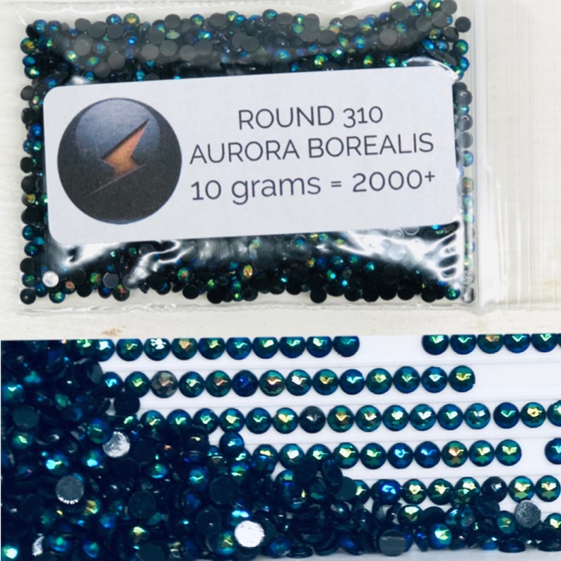 May include: A close-up of a bag of small, round, dark blue iridescent rhinestones. The bag has a label that reads "ROUND 310 AURORA BOREALIS 10 grams = 2000+".